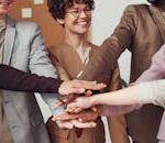 A group of happy, diverse colleagues celebrating teamwork and cooperation with a group high five indoors.