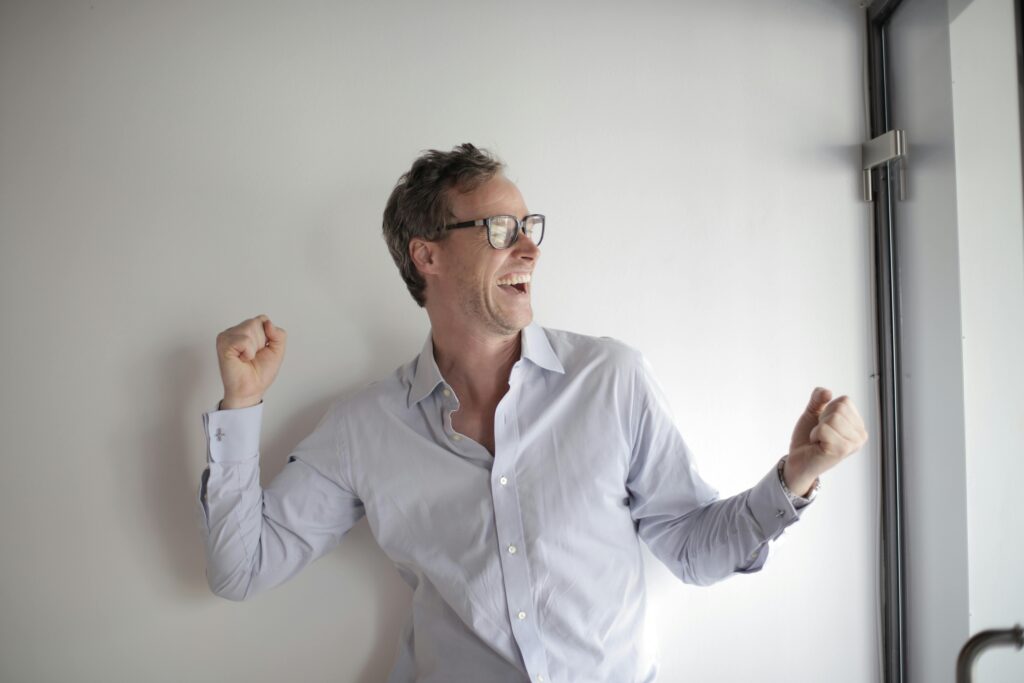 A smiling businessman in glasses celebrates a victory indoors, exuding positivity and joy.